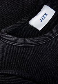 Zwarte ribstof met een gladde textuur, met een ronde halslijn en een label met "JJXX" in het blauw. Close-up weergave.