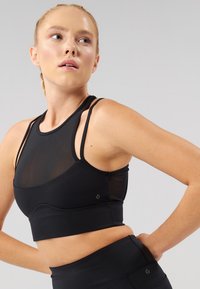 Sutien sport negru cu panouri din plasă, decolteu înalt și design elegant cu bretele subțiri. Textură netedă și siluetă mulată.