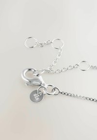 Ezüst nyaklánc kapocs homárfog zárral és "925" jelzésű medállal, vékony láncon, világos háttér előtt.