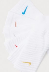 Valkoiset Nike-sukat, joissa on ribbiteksti, esittelevät värikkäitä logoja: sininen, oranssi, punainen ja kultainen. Ne on aseteltu tuuletinmalliseen järjestykseen.