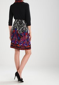 Top nero con maniche a tre quarti, abbinato a una gonna al ginocchio caratterizzata da un vivace motivo paisley con accenti rossi, blu e neri.