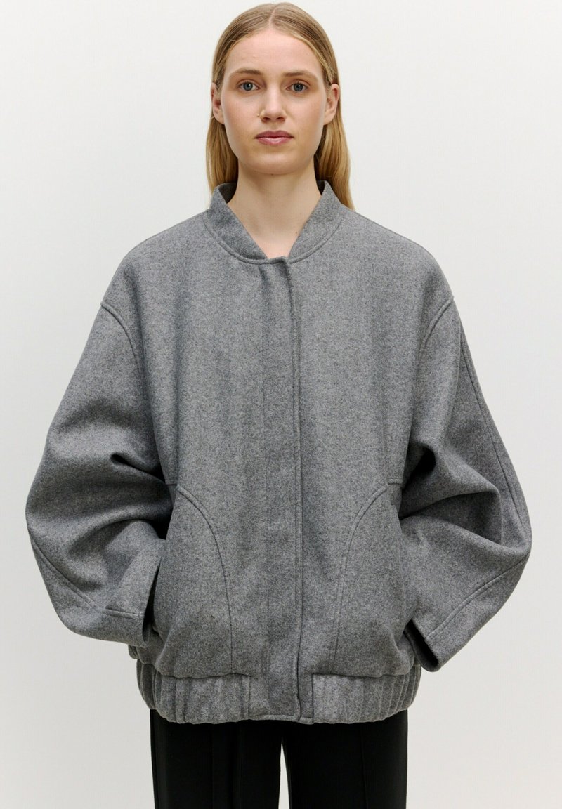 Grijze oversized wolmix jas met een hoge kraag, unieke naadaccenten en elastische manchetten. Heeft zijzakken en een relaxed fit.