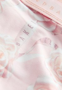 Tissu rose pâle avec un motif floral subtil et un texte discret "BAKER" imprimé dessus, montrant les détails de la texture et des coutures.