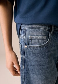 Traperice svijetlo plave boje s teksturiranim završetkom, s stražnjim džepom, detaljem zakovice i blago suženim krojem.