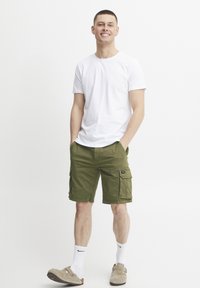 Weißes T-Shirt mit kurzen Ärmeln, olivgrüne Cargo-Shorts mit seitlichen Taschen und beiges Slip-On-Schuhe mit weißen Socken. Sauberer, lässiger Look.