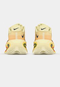 Αθλητικά παπούτσια Nike με επάνω μέρος από ανοιχτό κίτρινο πλέγμα, αντίθετο μπλε σήμα Swoosh και λαστιχένια σόλα με πολύχρωμες λεπτομέρειες στη φτέρνα.