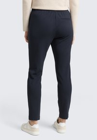 Marintröjor med en tapered passform, elastiskt midjeband och detalj på bakfickan, kombinerat med vita och beige sneakers. Mjukt material, slät textur.