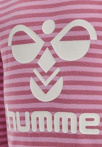 Stribet pink t-shirt med et stort hvidt logodesign og mærkenavnet "humme" med fed skrift. Blød stoftekstur med en tætsiddende pasform.