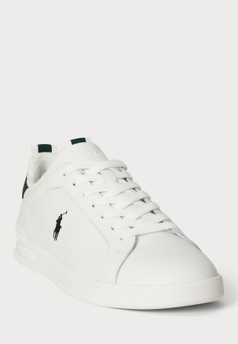 Sneaker bianco in pelle con superficie testurizzata, lacci piatti e accenti verdi. Presenta un logo nero su un lato e un collo imbottito per maggiore comfort.