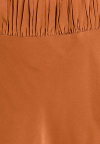 Tessuto terracotta con una trama liscia e un dettaglio arricciato nella parte superiore, caratterizzato da un colore solido senza motivi o accessori.