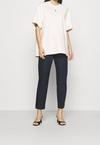 Krämfärgad oversize T-shirt med korta ärmar, kombinerad med slim fit mörkblå byxor och svarta remsandaler. Minimalistisk design, slät textur.