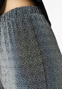 Melnas un sudrabainas rakstainas audums ar savītās jostasvietas detalizējumu, kurai ir fakturēts, austs dizains un viegla spīduma efekts.