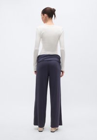 Ivoriju krāsas tops ar garām piedurknēm un apaļu kakla izgriezumu, kombinēts ar tumši violetām, platajiem biksēm ar elastīgu jostasvietu un savākumu jostasvietā.