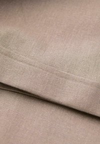 Gros plan d’un tissu beige tissé montrant la texture détaillée et la couture le long d’un bord plié.