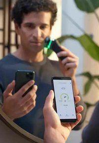 Dispositivo facciale elettrico con un design nero e verde, che mostra un'interfaccia a schermo in una mano. Smartphone con l'app aperta nell'altra mano, superficie riflettente.