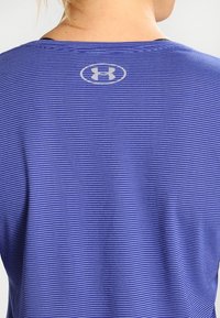 Lila randig idrottströja med rund halsringning, med Under Armour-logotypen i en ljus färg på baksidan. Mjuk tygtextur.