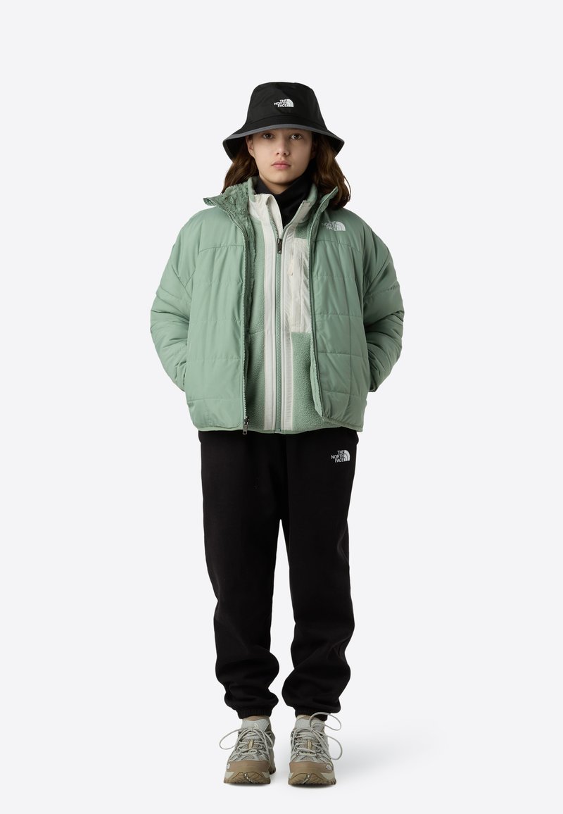 Mintgrøn puffjakke lagdelt over en hvid fleece, sorte joggingbukser og en sort bucket hat. Grå og beige sneakers fuldender outfittet.