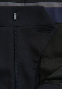 Schwarzer Sportbekleidungsstoff mit glatter Textur, ausgestattet mit einem Reißverschluss, einem kleinen Metallelement und kontrastierenden dunklen Paneeldetails.
