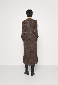 Robe florale noire avec de longues manches bouffantes, un ourlet à volants et un corsage ajusté. Présente de petites fleurs rouges et vertes dans tout le motif.