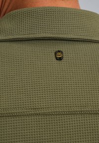 Donkergroene, gestructureerde stof met een wafelpatroon, voorzien van een zwarte en gouden "PME Legend" label dat zich aan de bovenrug bevindt.