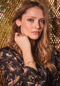 Aukso grandinėlė su mėlynais akmenimis, dėvima ant riešo. Modelis tamsiu gėlių bluzonu, su gyvūnų ir augalų mišiniu. Tekstūruota fonas.