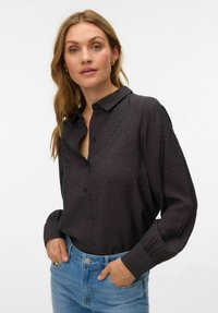 Mustast kangast lukkudega särgi, millel on esiküljel laiali laotud tekstureeritud kangas ja rhinestone-kaunistused. Pikal varrukal on mansetiga detailid.