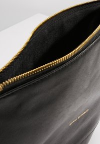 Pochette en cuir noir avec fermeture éclair dorée partiellement ouverte, montrant une doublure en tissu noir et un petit logo doré "Royal Republic" à l'extérieur.