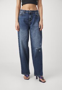 Højtaljede, løstsiddende blå denimjeans med en slidt finish og distressed detaljer. Har fem lommer og lynlås.