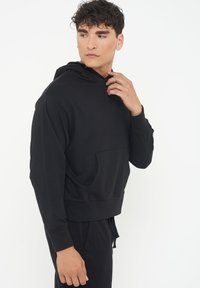 Black hooded sweatshirt with a kangaroo pocket, soft fabric, relaxed fit, ribbed cuffs, and a drawstring at the hem.