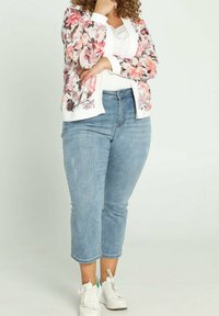 Cardigan con estampado floral en rosa y blanco, combinado con unos vaqueros recortados en azul claro y zapatillas blancas. El material es suave, casual y cómodo.