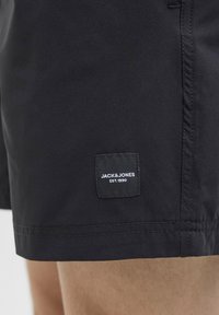 Pantalones cortos negros de tela suave, con un dobladillo cosido y un parche de logo cuadrado en el lateral con "JACK & JONES EST. 1990."