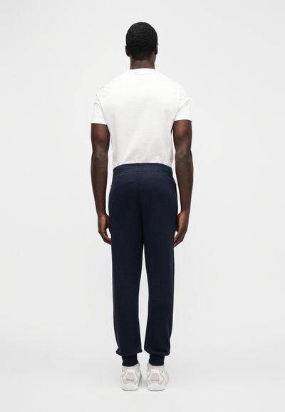 Marineblauwe joggingbroek met elastische tailleband, ruime pasvorm en omgeslagen enkels, gecombineerd met een effen wit T-shirt en witte sneakers.