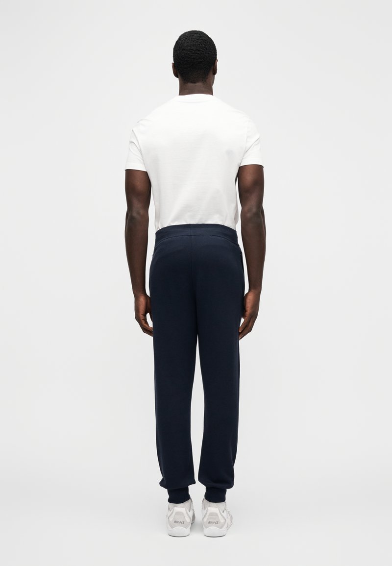 Marinblå joggingbyxor med elastisk midja, avslappnad passform och mudd vid anklarna, kombinerade med en enkel vit t-shirt och vita sneakers.