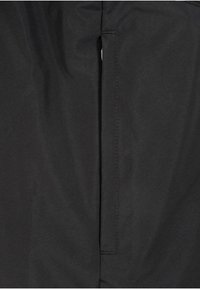 Czarny materiał z pionowym szwem i wąską, prostokątną kieszenią na prawym boku.