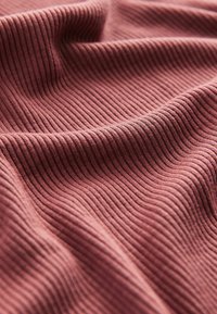 Texturerad, ribbad väv i en dämpad rosfärg; mjukt material med framträdande vertikala linjer och mjuka veck som skapar djup och rörelse.