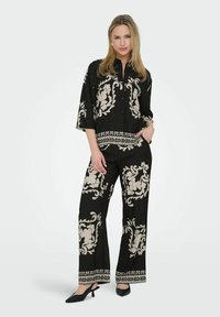 Ensemble noir à deux pièces comprenant une chemise à manches longues et un pantalon à jambes larges. Des motifs floraux crème ornent les deux pièces, avec une finition décorative le long de l'ourlet.