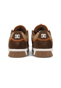 Hnedé semišové tenisky s svetlohnedými sieťovinovými detailmi a oranžovými akcentmi. Biela gumová podrážka s textúrovaným gripom. Logo DC na päte a boku.