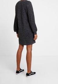 Mörkgrå stickad klänning med långa, puffiga ärmar, rundad halsringning och en något oversized silhuett; bärs med svarta sneakers.