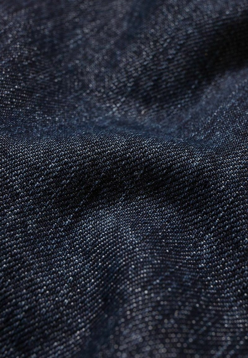 Tissu en denim bleu marine avec une texture lisse et un léger éclat, présentant un motif de tissage diagonal et des variations de couleur subtiles.