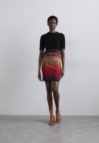 Vestido de malha com mangas curtas; parte superior preta a transitar para um padrão de ziguezague multicolorido em vermelho, rosa e amarelo; combinado com botas de tornozelo em tom bege.