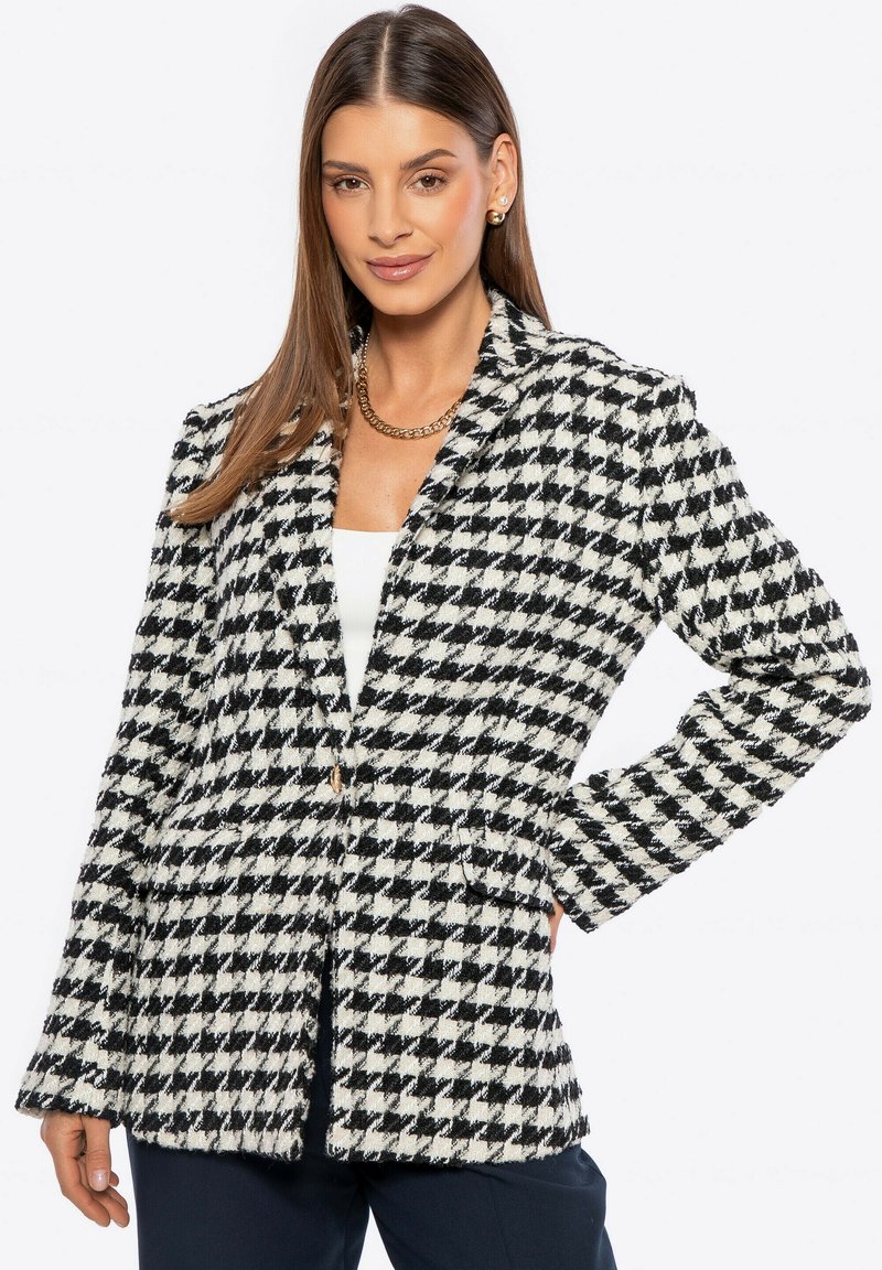 Blazer en blanco y negro con patrón de espiga, hecho de tejido texturizado, con cierre de un solo botón y dos bolsillos frontales. Ajuste estructurado y entallado.