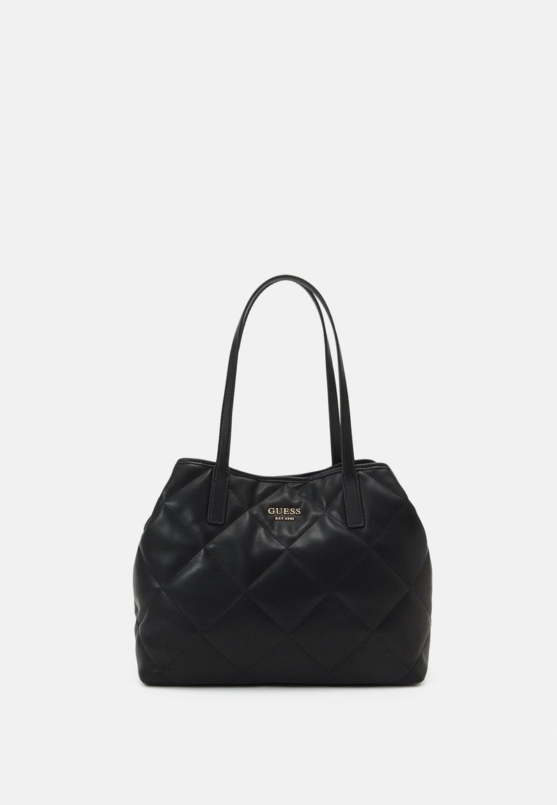 Sac fourre-tout en cuir noir matelassé avec double anse d'épaule et petit logo doré "GUESS EST 1981" au centre avant.