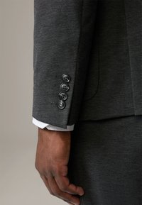 Mankiet ciemnoszarej marynarki z czterema czarnymi guzikami, z białym mankietem koszuli wystającym na zewnątrz. Tkanina ma subtelną, teksturowaną strukturę.