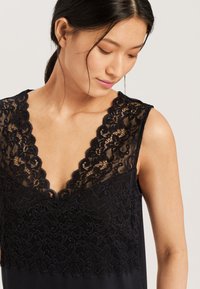 Top navy con sovrapposizione in pizzo con motivo floreale, scollatura a margine ondulato e design senza maniche. Tessuto liscio con silhouette aderente.