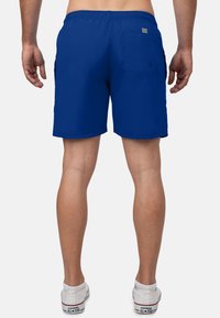 Blauwe korte broek voor heren van soepel materiaal, met een elastische tailleband en een achterzak met een vierkante accent. Kort boven de knie.