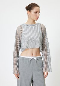 Grijze cropped lange mouwen top gemaakt van gaasstof met grote gaten. Gecombineerd met lichtgrijze gestreepte broek met een trekkoord in de taille.