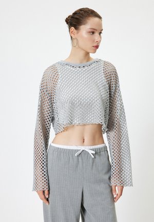 Grijze cropped lange mouwen top gemaakt van gaasstof met grote gaten. Gecombineerd met lichtgrijze gestreepte broek met een trekkoord in de taille.