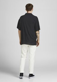 Pantalones blancos combinados con una camiseta negra de manga corta y ajustada. La camiseta tiene un cuello; tatuajes visibles en el brazo. Zapatos negros con detalles blancos.