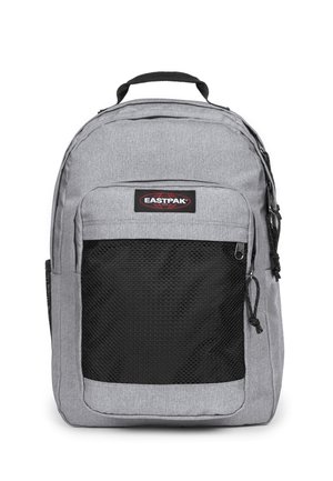 Mochila de nylon gris con un bolsillo frontal de malla negra, asa en la parte superior y correas de hombro ajustables. Presenta un logotipo de marca Eastpak.