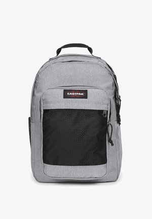 Mochila de nylon gris con un bolsillo frontal de malla negra, asa en la parte superior y correas de hombro ajustables. Presenta un logotipo de marca Eastpak.